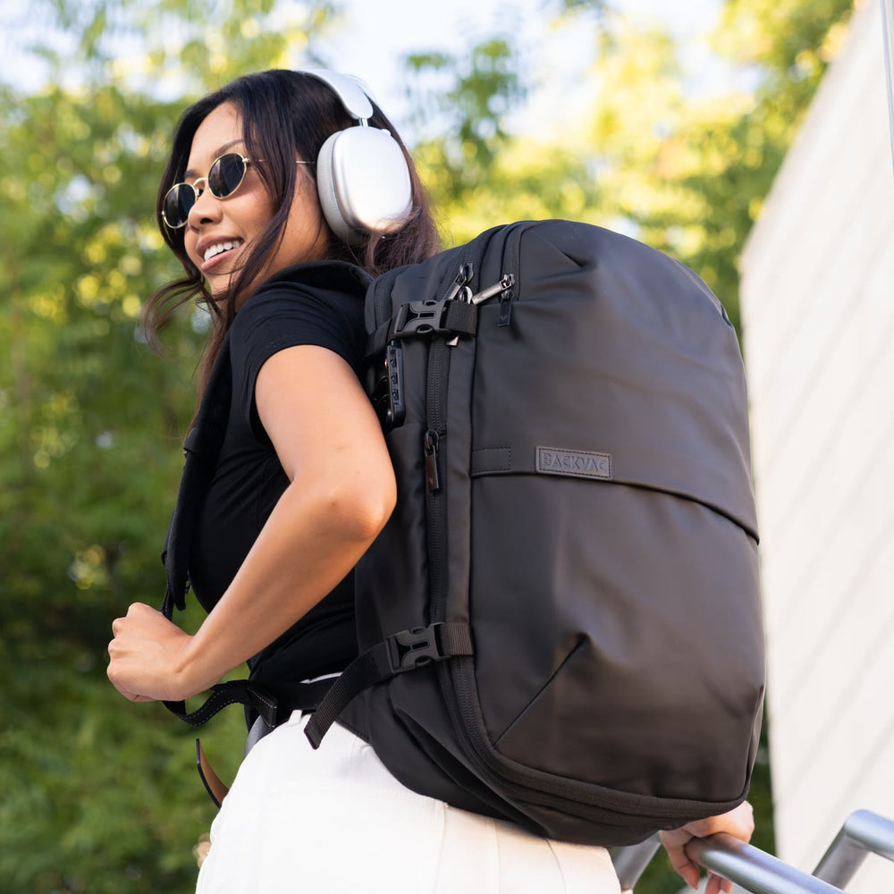 木々を背に、屋外の階段でマットブラックの Backvac Pro を背負う女性
