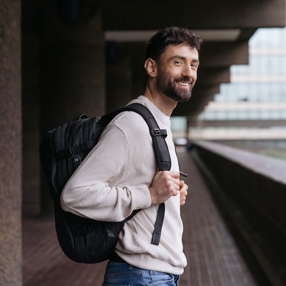 コンクリートの列柱が並ぶ通路で、マットブラックの Backvac Pro を背負う男性