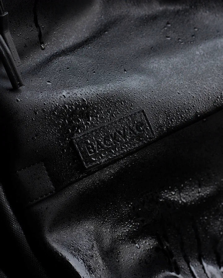 黒の Backvac Pro の生地、BACKVAC パッチの横で水滴が玉になっている様子のクローズアップ